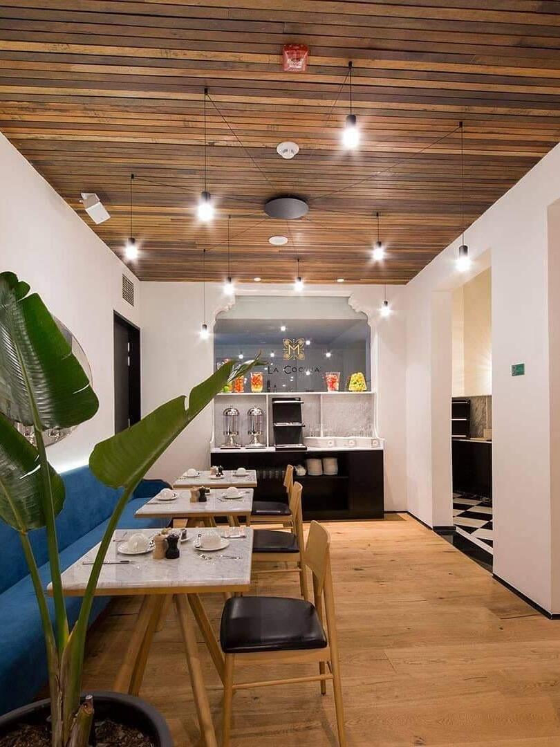 Small lit pendants along a wood ceiling above restaurant tables and chairs