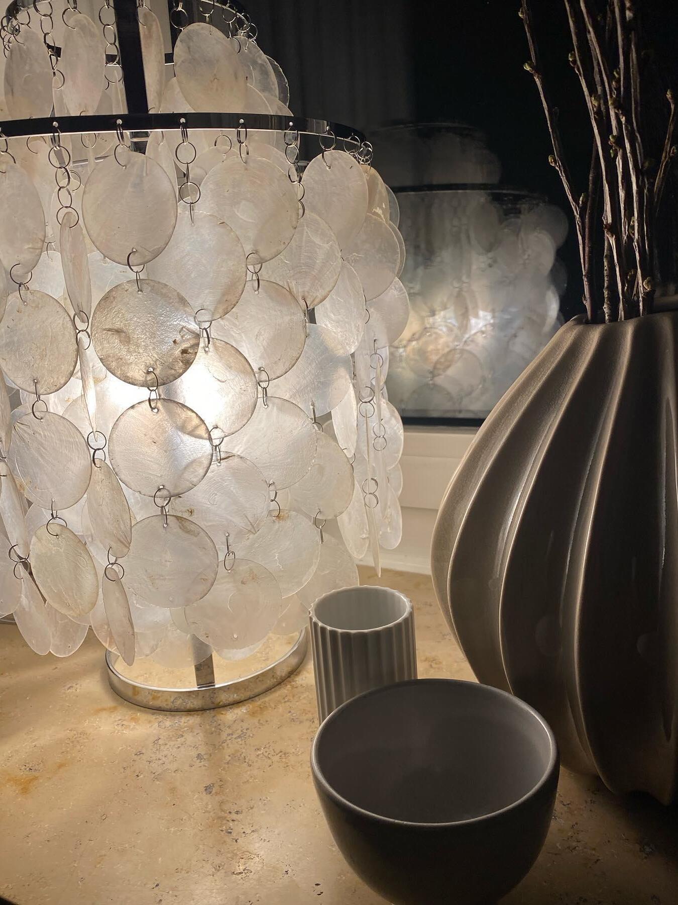 Lit shell lamp beside dark bowl and tall vase