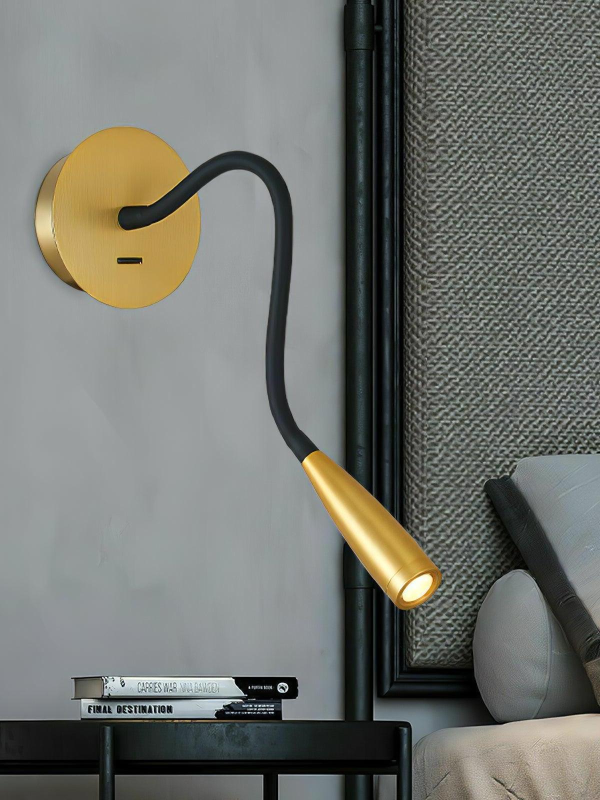 Gold Flexi above a black bedside table and books beside a grey headboard, with plate switch and lit tapered head