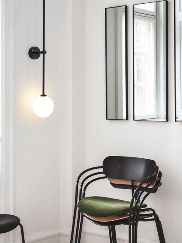 Black rod wall light with a glowing white globe beside a black chair and three narrow wall mirrors