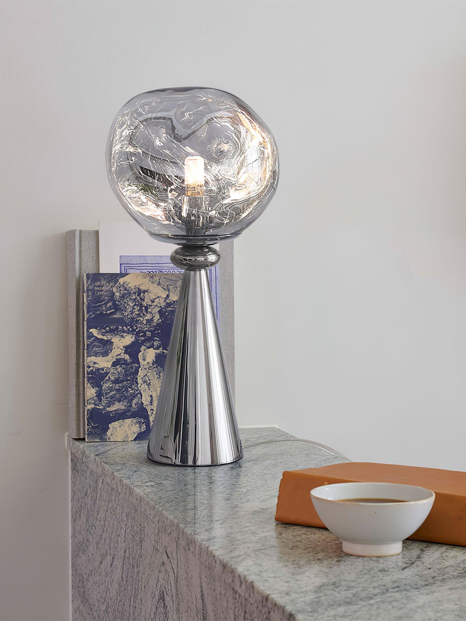 Chrome globe table lamp on a stone surface beside a blue book, orange book and white cup