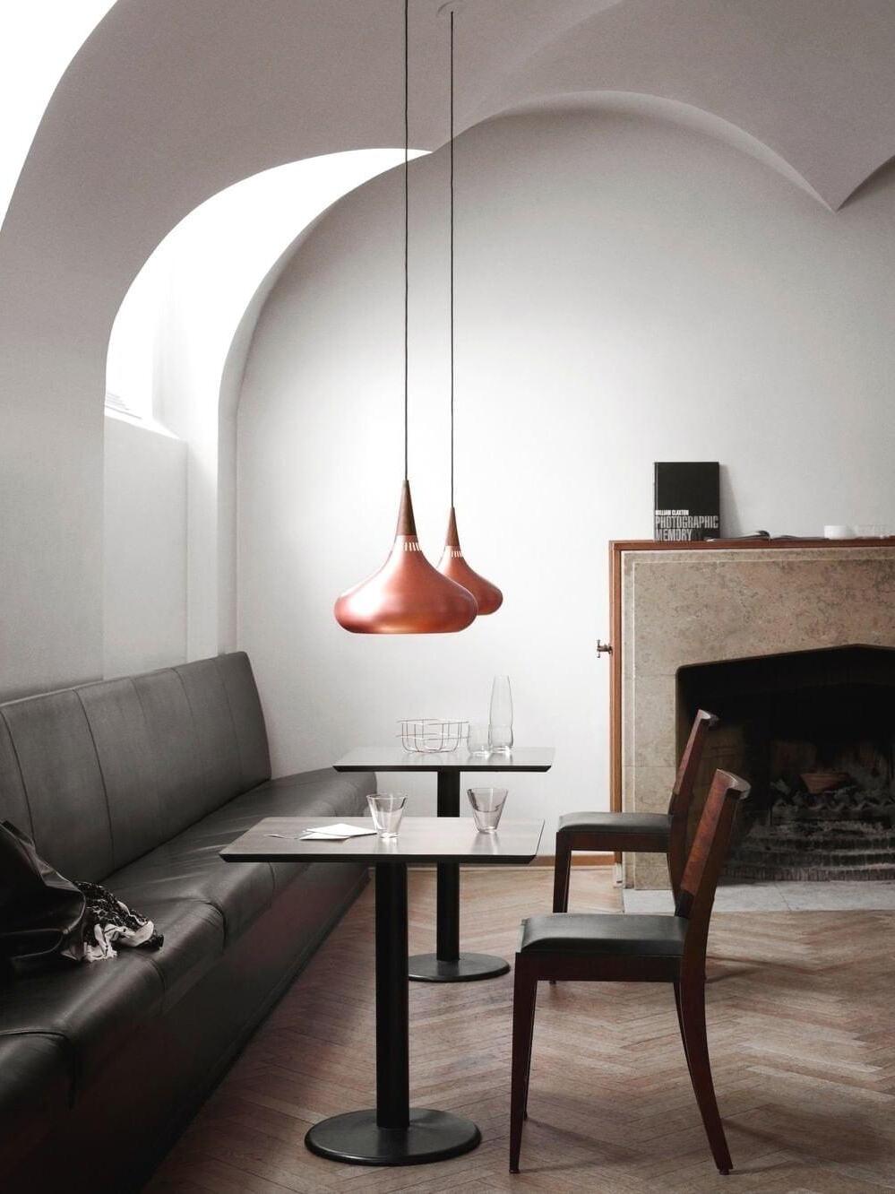 Two Copper pendants above small square tables beside a curved dining alcove