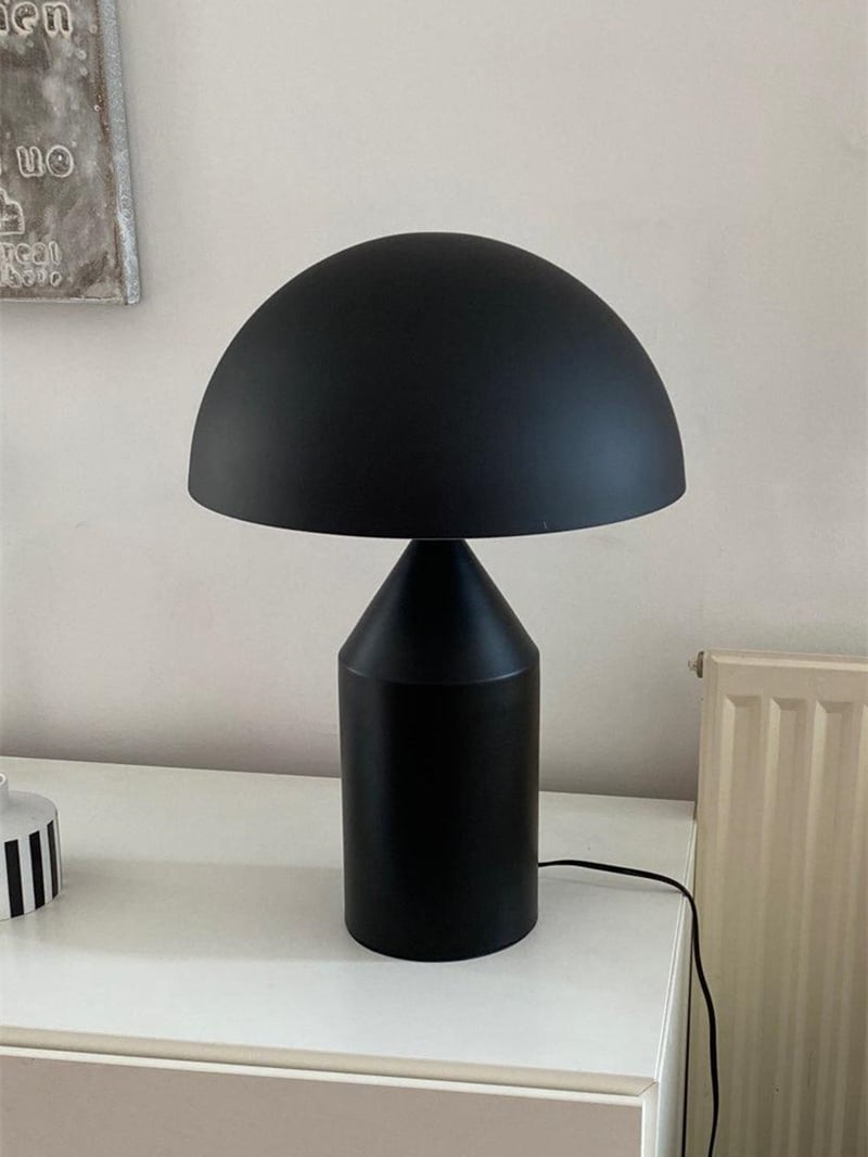Matte-looking black dome table lamp with a power cable on a white cabinet beside a radiator
