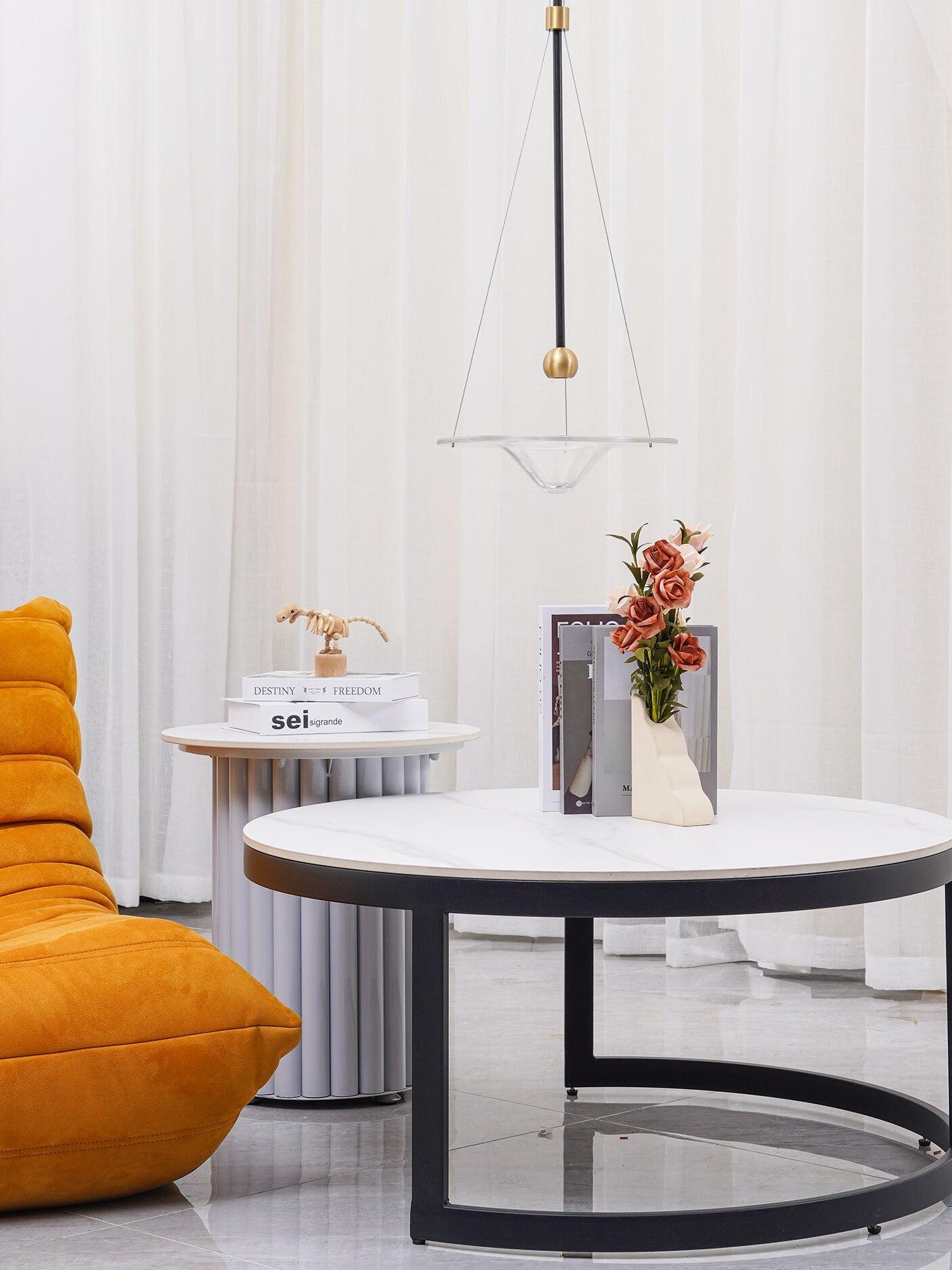 Clear glass disc above round table by orange chair