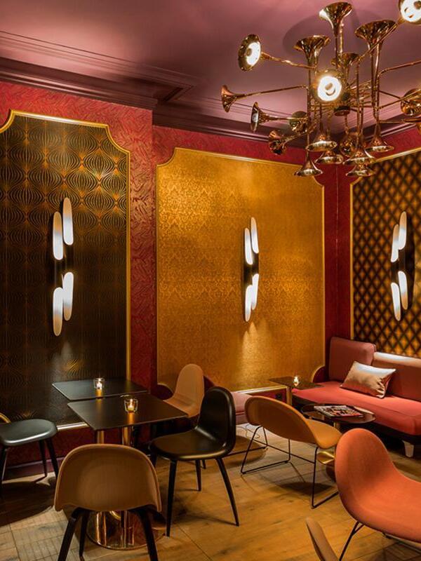 Twin-tube wall sconces on red-and-gold patterned lounge walls with tables, chairs and a separate horn-shaped chandelier