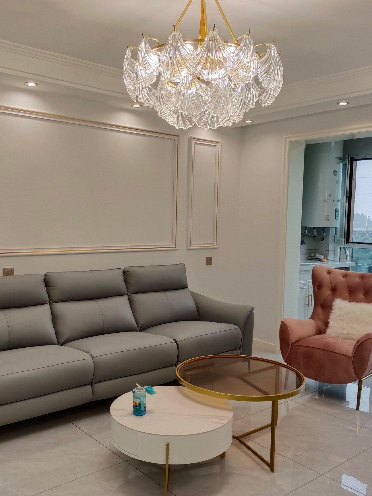 Glass ceiling light in a living room with a gray sofa, pink tufted chair and round tables