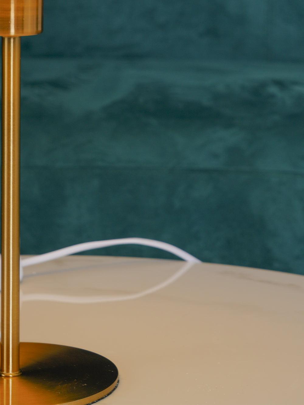 Close-up of the slim gold-tone stem meeting the round disk base, with a white cable behind