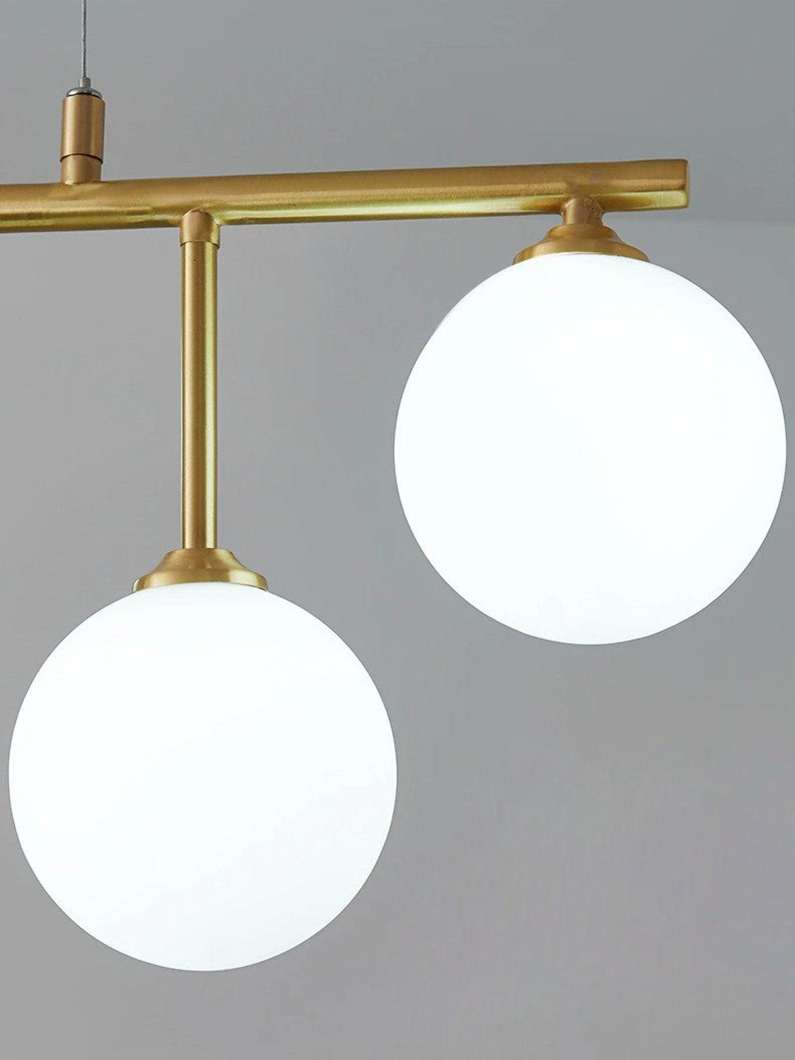Close view of two white glass globes hanging at different heights below an Arteriors brass-tone bar