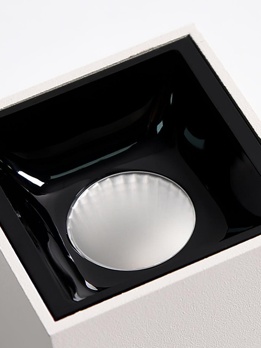 Macro view of a glossy black square recessed cup and circular reflector inside a white housing