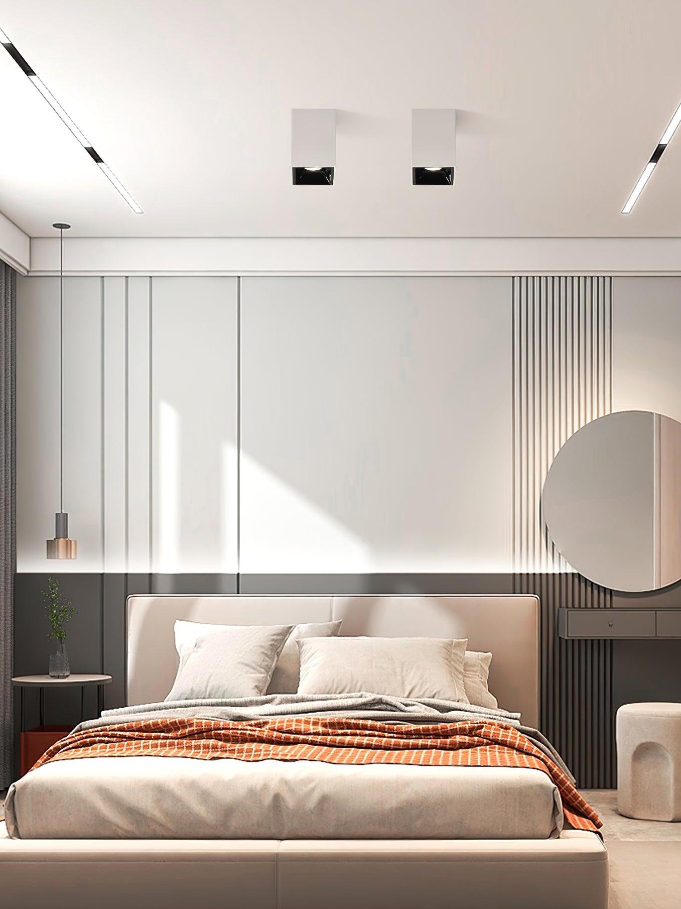Two white ceiling spots with black recesses above a bed, tan headboard and round mirror