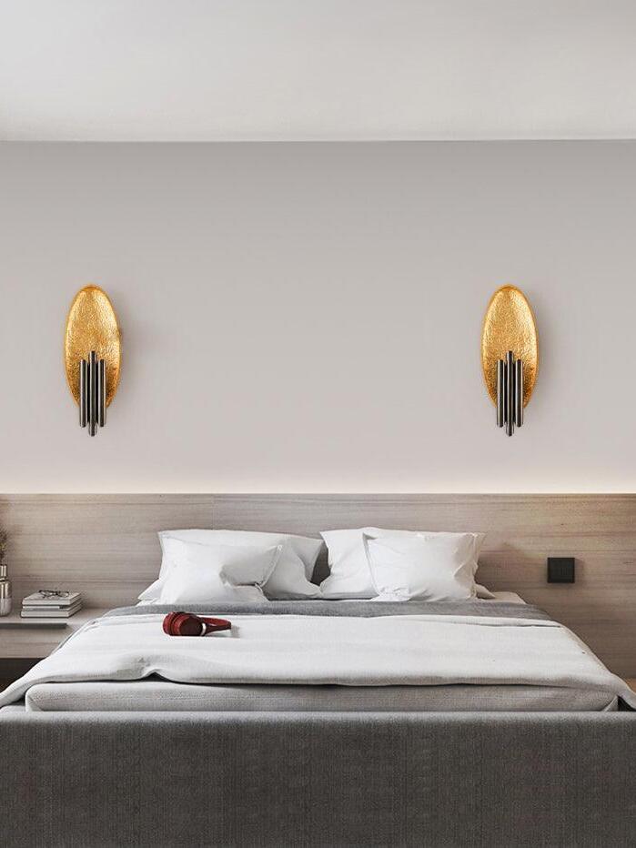 Matching gold-tone oval and dark-tube sconces above bed headboard