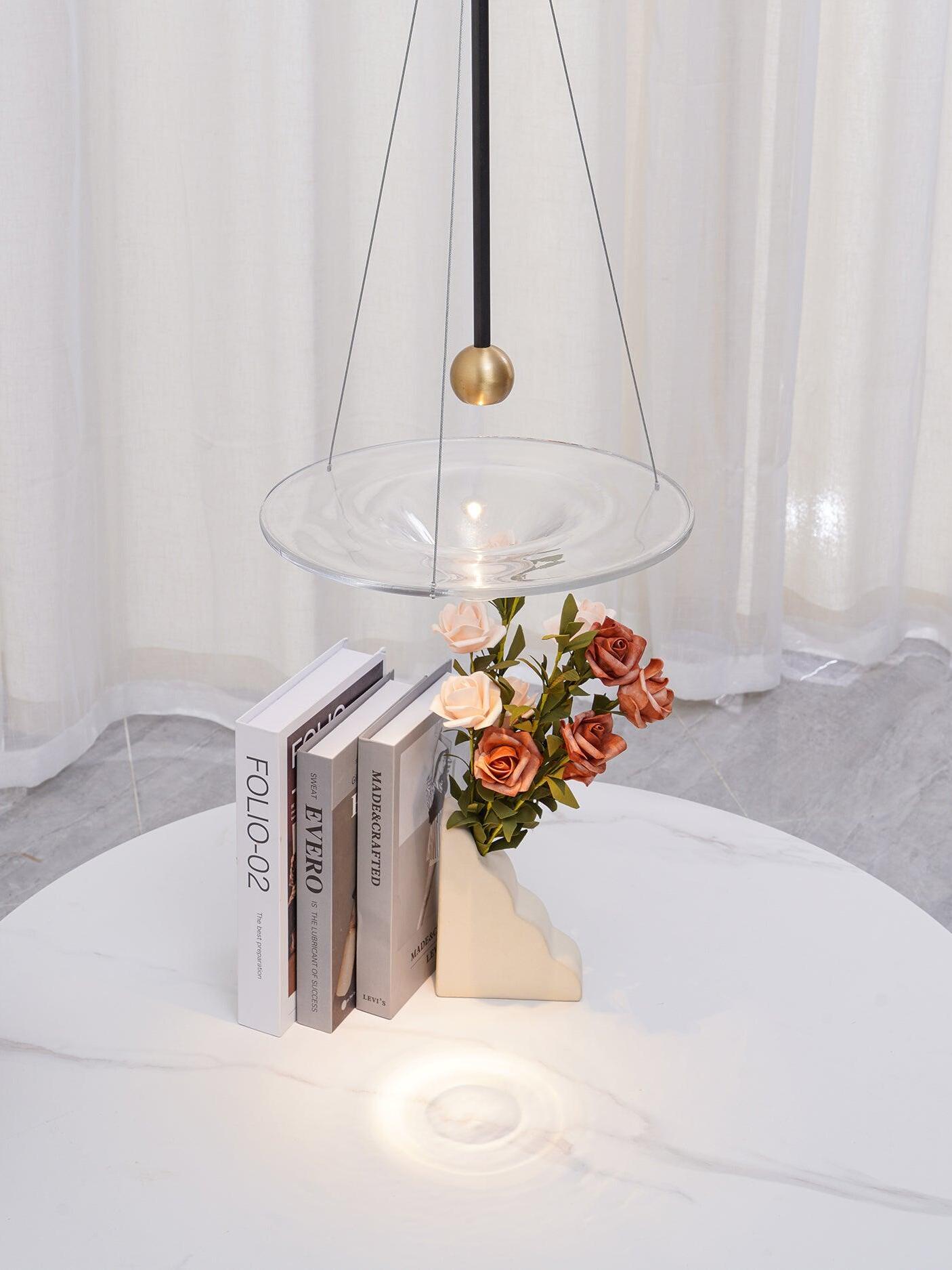 Glass disc pendant and brass ball over books and flowers