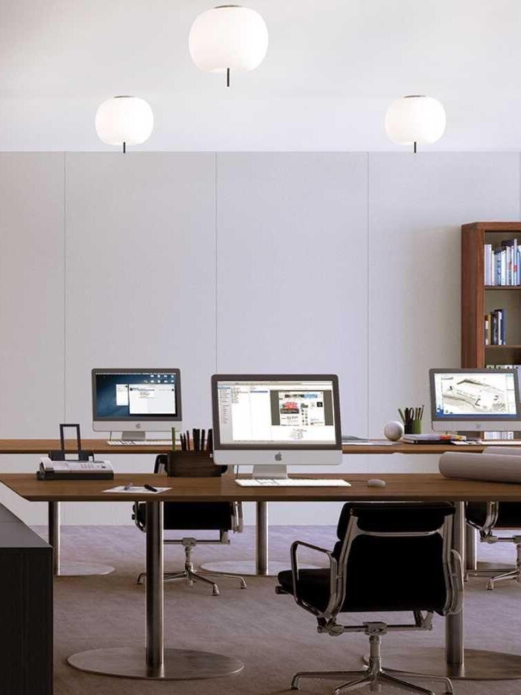 Three illuminated white ceiling shades above shared office desks and computer screens