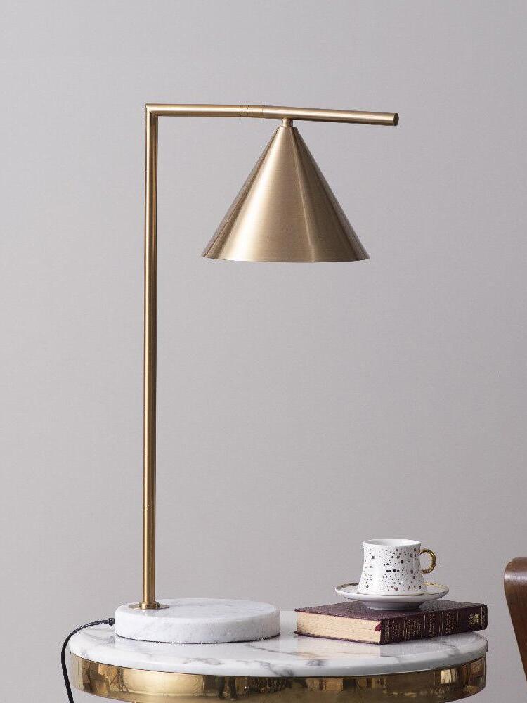 Gold-tone cone table lamp with cup and books on round table