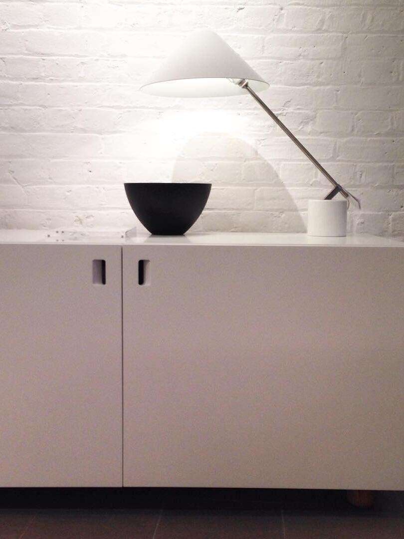 Lit white table lamp beside a black bowl on a cabinet against white brick