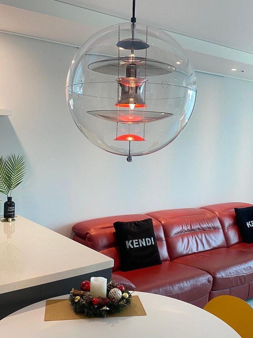 Lit clear globe pendant above a white dining table beside a red leather sofa