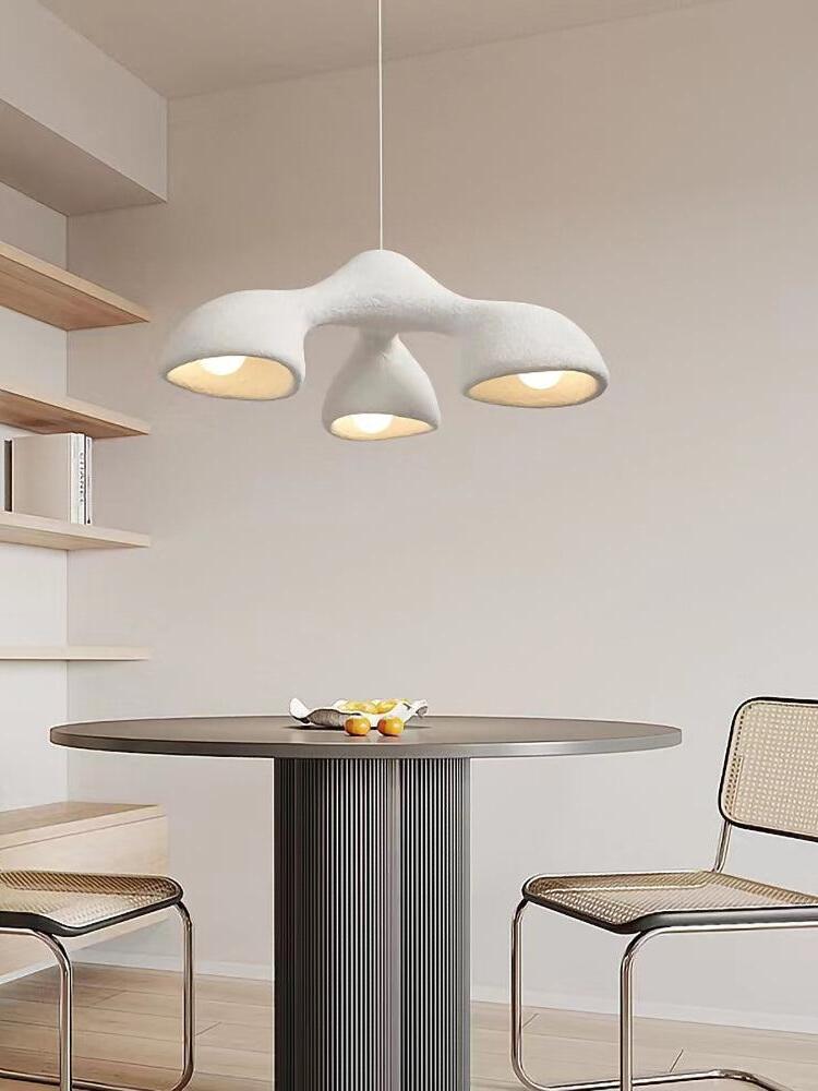 Compact white three-opening pendant above a round dark dining table with fruit, cane chairs and shelves