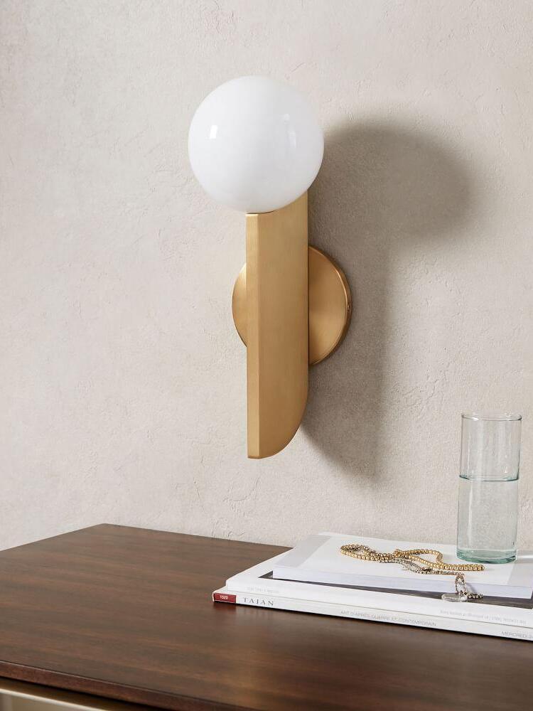Unlit white globe wall lamp with gold-colour blade above books and a water glass