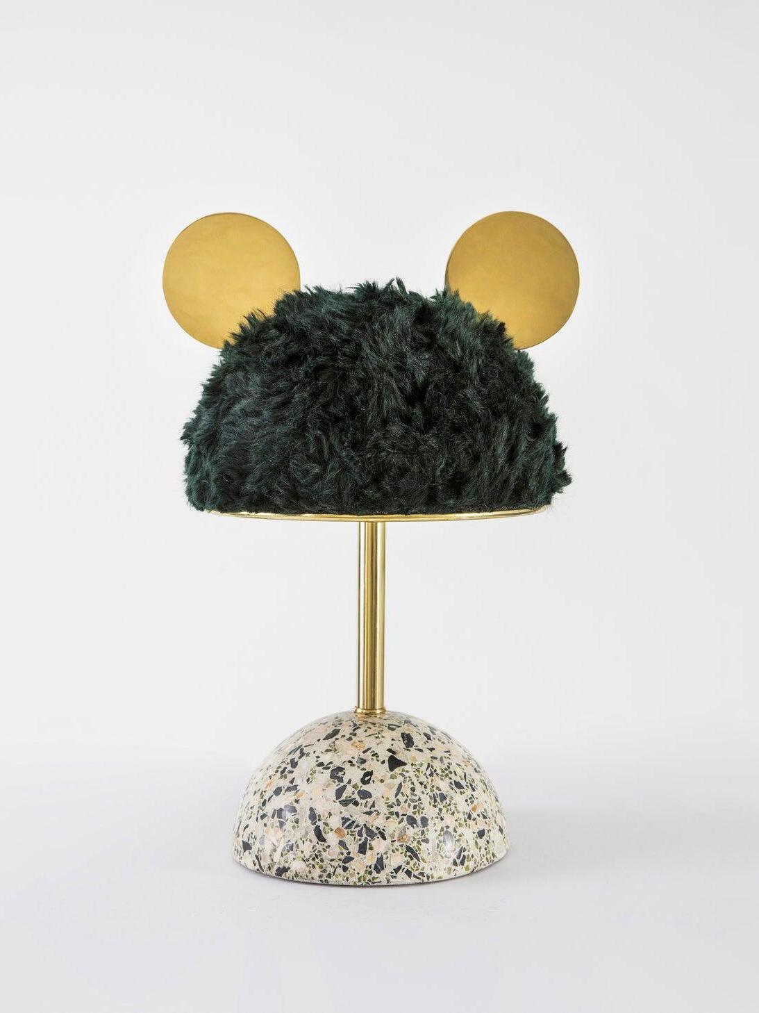 Dark green plush shade above black-white speckled base with gold-tone stem and discs