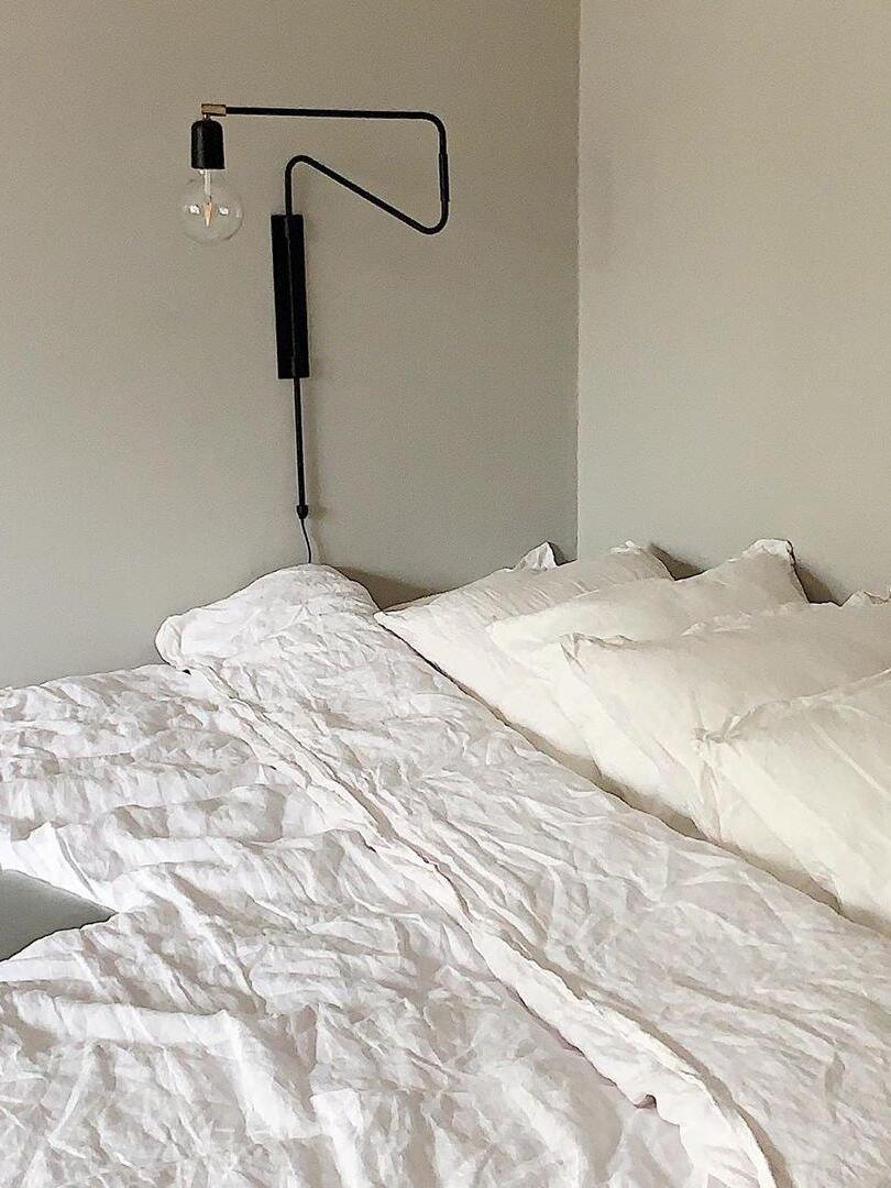 Black wall lamp with bent arm turned left and clear globe bulb above white bedding