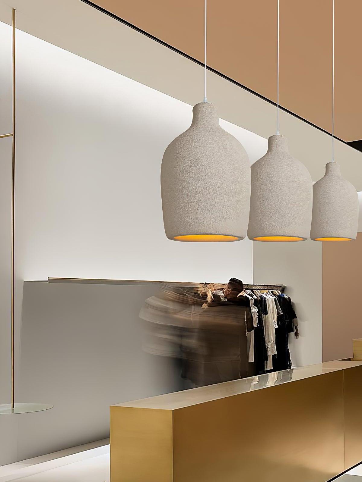 Three separate textured bottle pendants above a gold-coloured clothing-shop counter and clothes rail