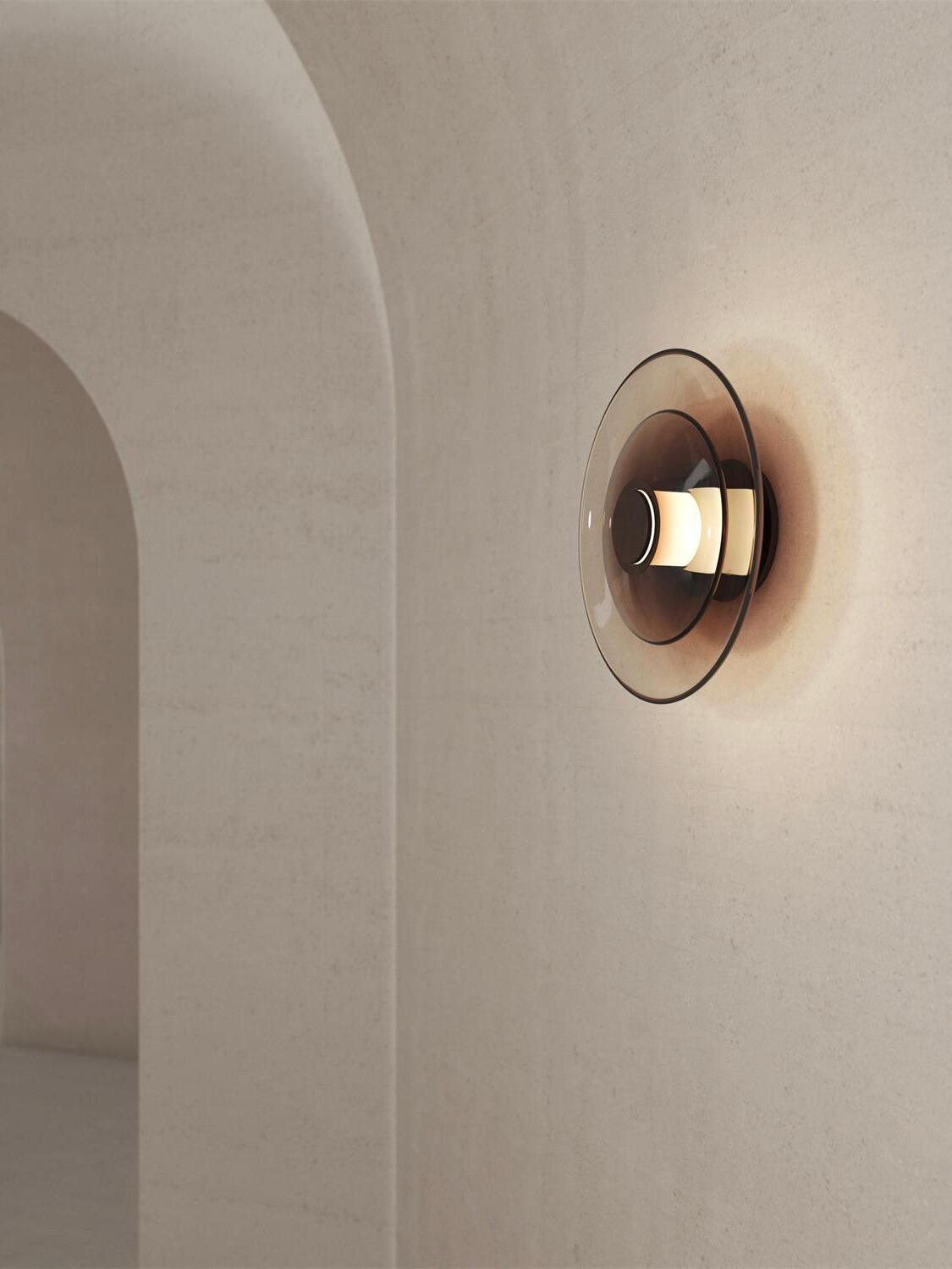 Dark glass-disc wall light glowing against plaster arch