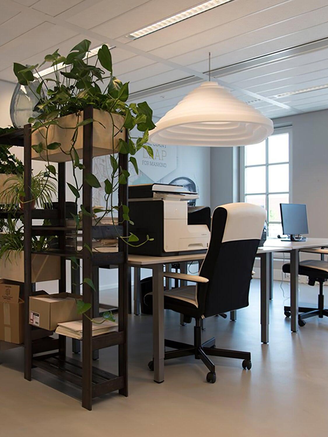 White stepped pendant over an office workspace beside shelving and trailing plants.