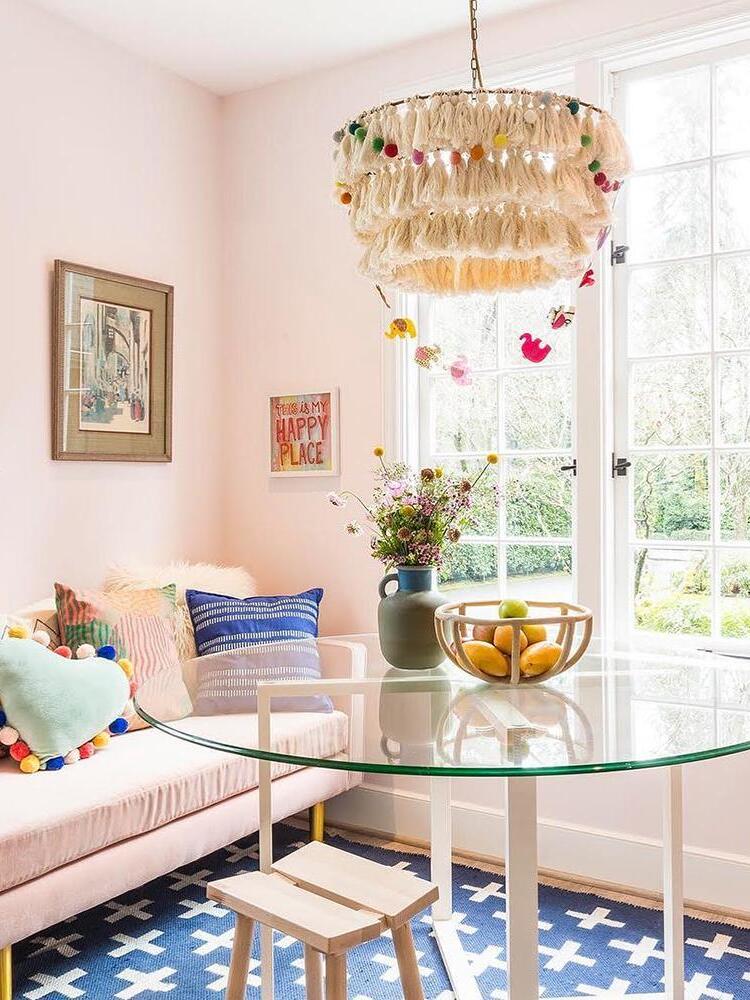 Cream tassel chandelier with colourful ball decorations above a glass table in a pink room with fruit and flowers