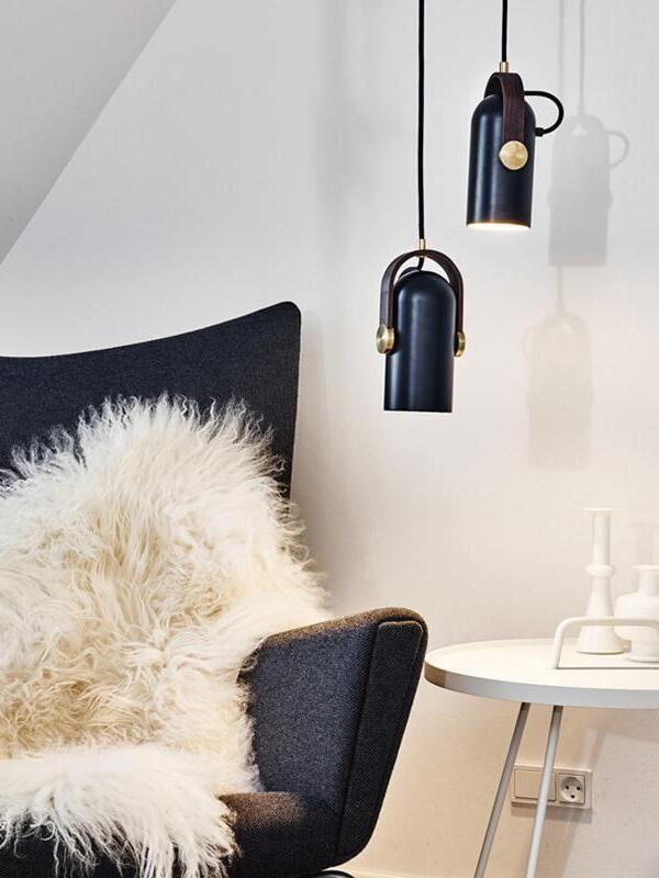 Two black pendants beside a dark upholstered chair with white sheepskin and a round white side table