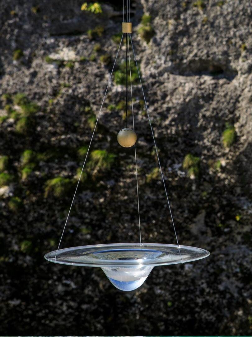 Glass disc pendant pictured before rugged rock face