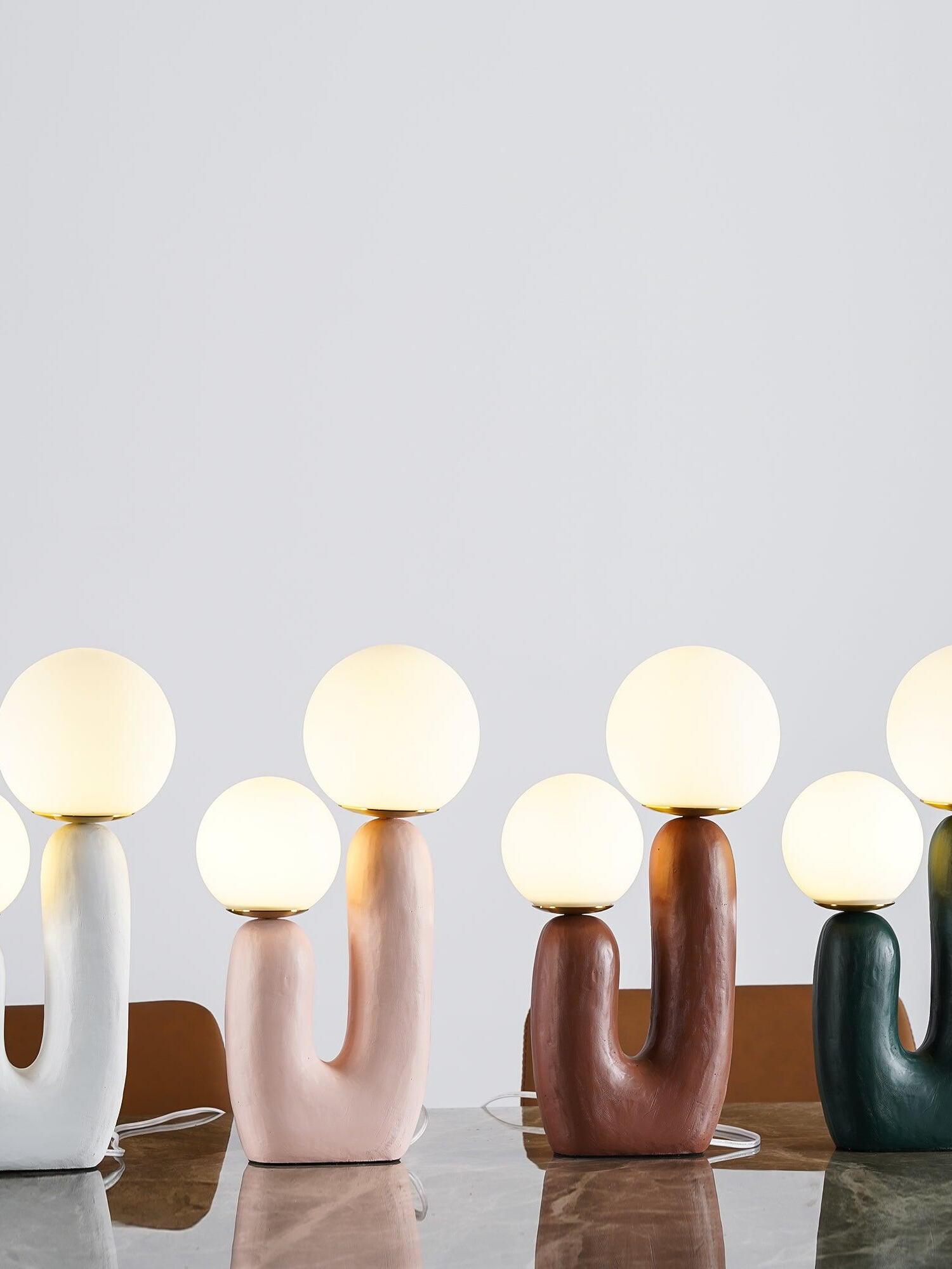 White, pink, terracotta and green Oo Rough lamps in a row on marble, their opal globes glowing warm-looking