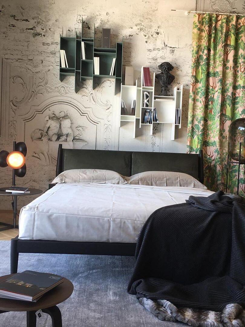 Dark glass lamp among framed wall art near a bed.
