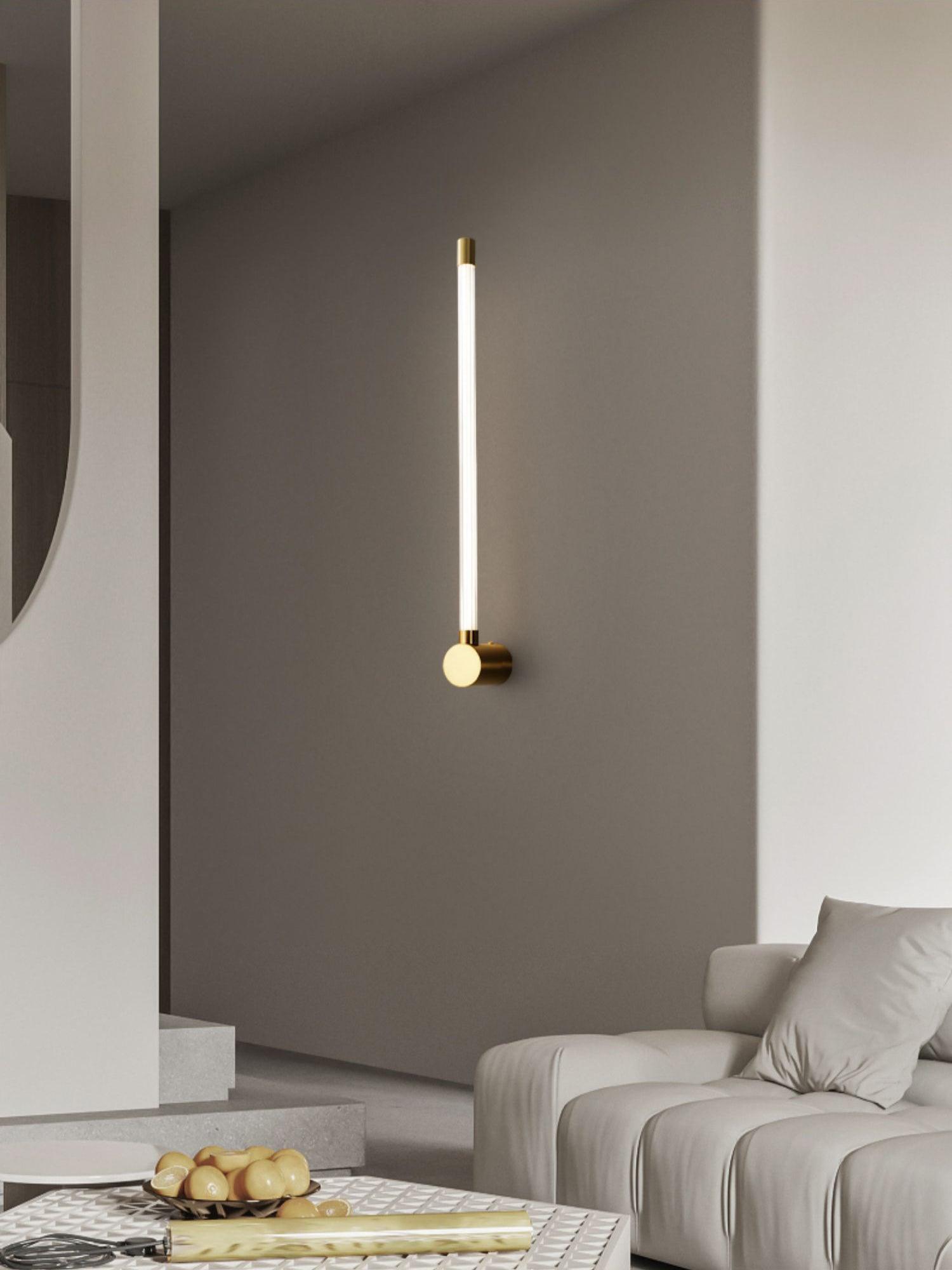 Brass-tone single-tube sconce on a gray wall above a coffee table beside a pale sofa