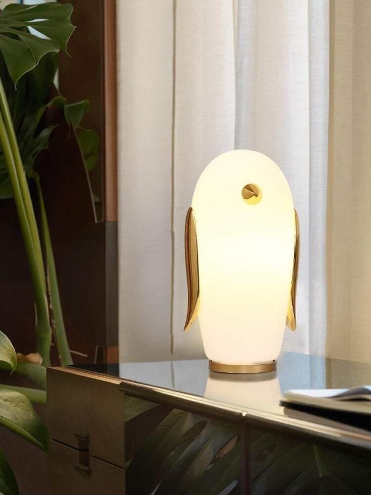Lit tall penguin lamp on dark cabinet beside window and plant