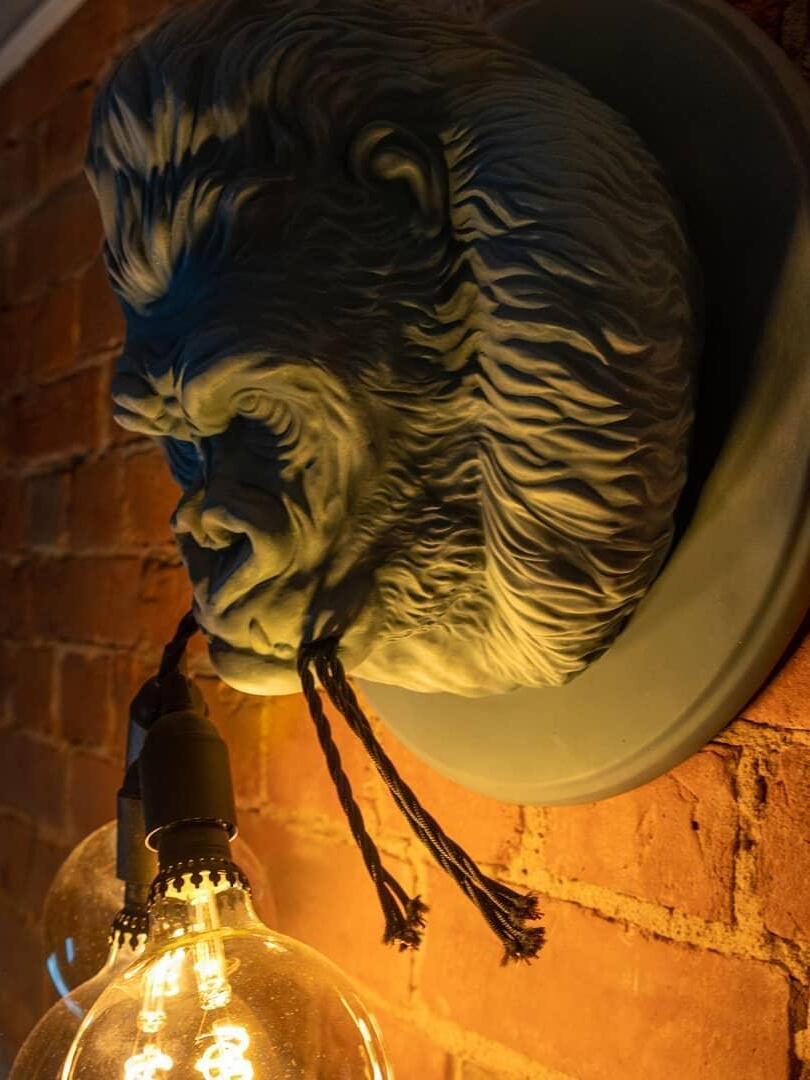 Warm-lit grey gorilla relief with bulb and jaw cords on brick wall