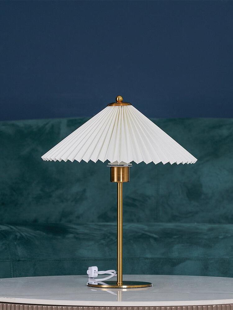 Unlit Perla table lamp on a white round table in front of a green upholstered sofa
