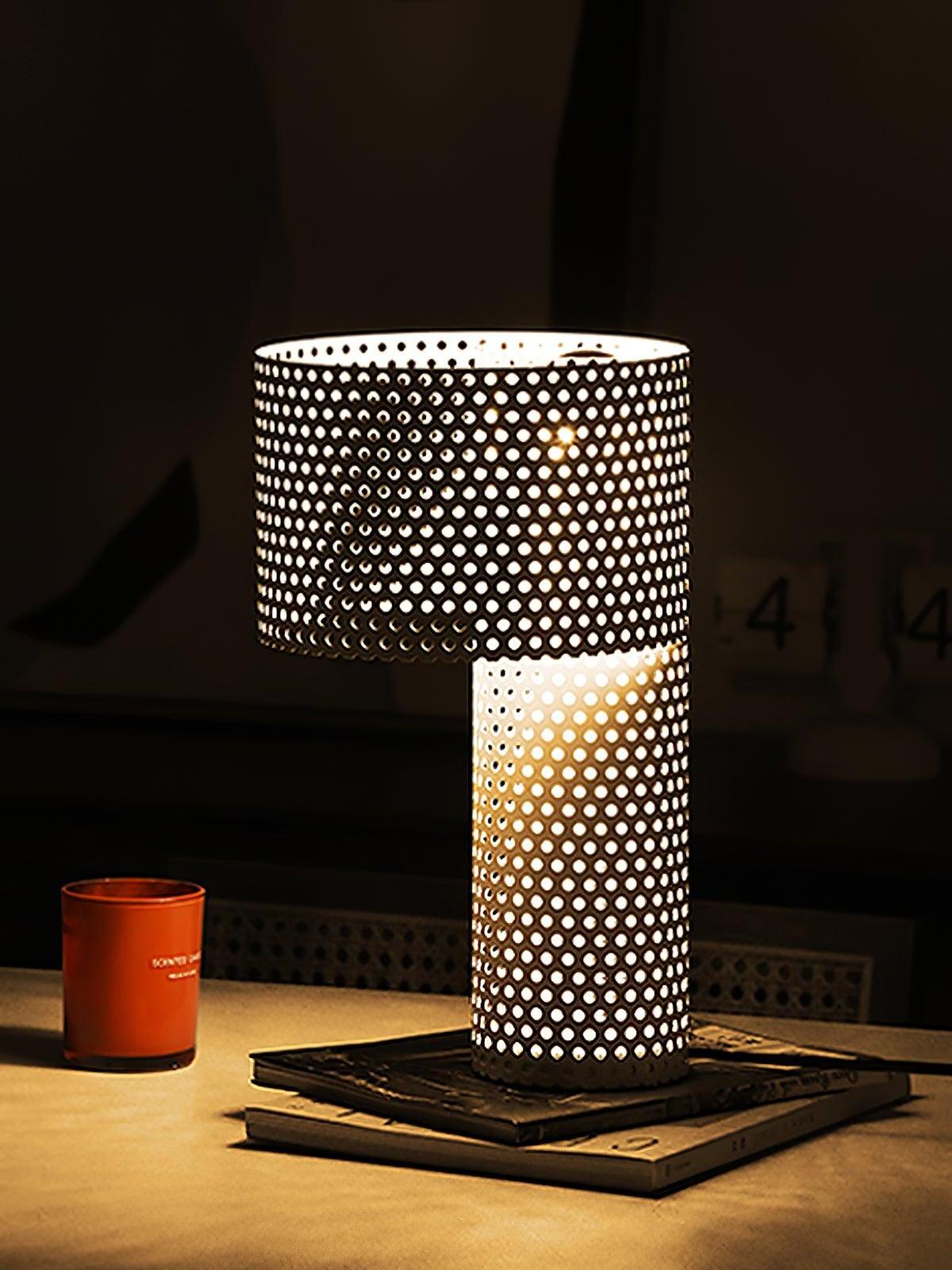 Lit white perforated lamp on books against dark wall
