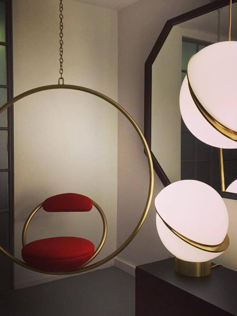 Cropped Crescent pendant near a separate globe table lamp, mirror and circular hanging chair with a red cushion