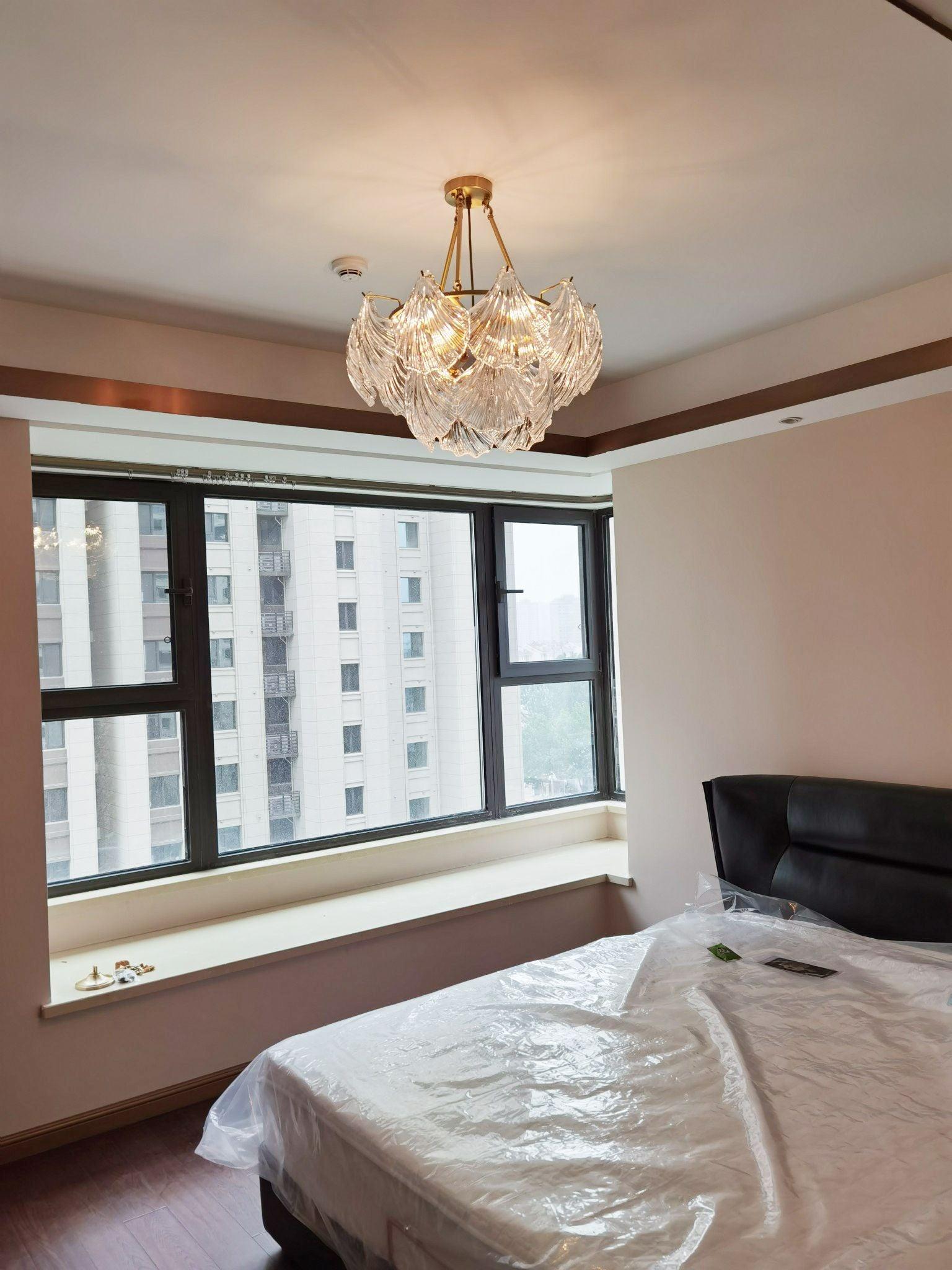 Shell-panel ceiling light above a pink bedcover beside a wide window
