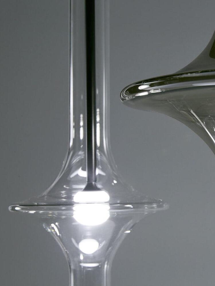 Clear flared glass shade with dark central stem and glowing light point beside a cropped smoky shade