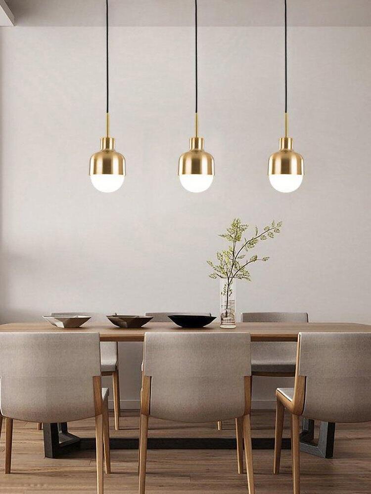 Three separate lit Niku pendants above a wooden dining table with bowls, flowers and upholstered chairs