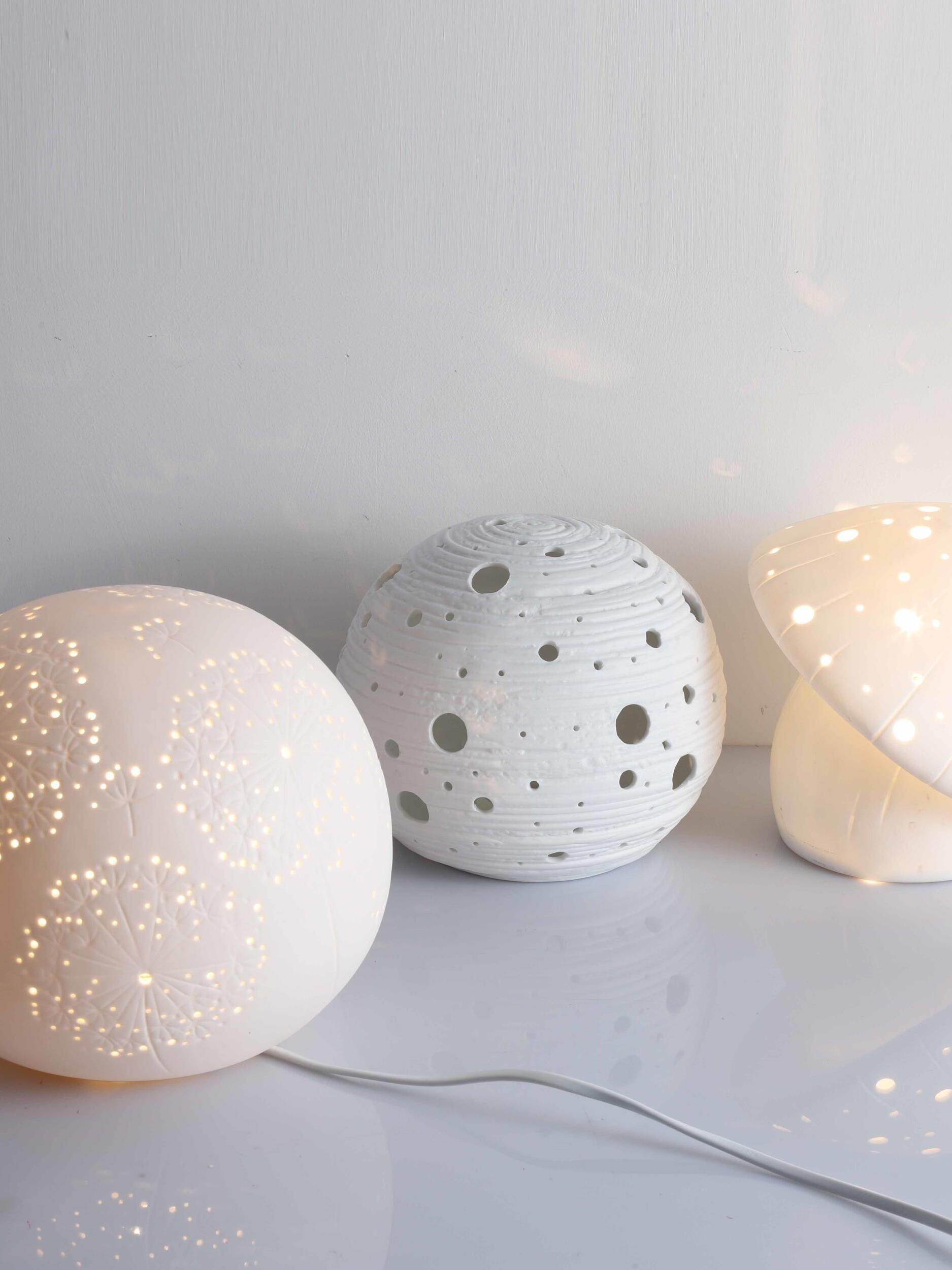 Round perforated lamp with a cable beside an unlit round lamp and part of a lit mushroom lamp
