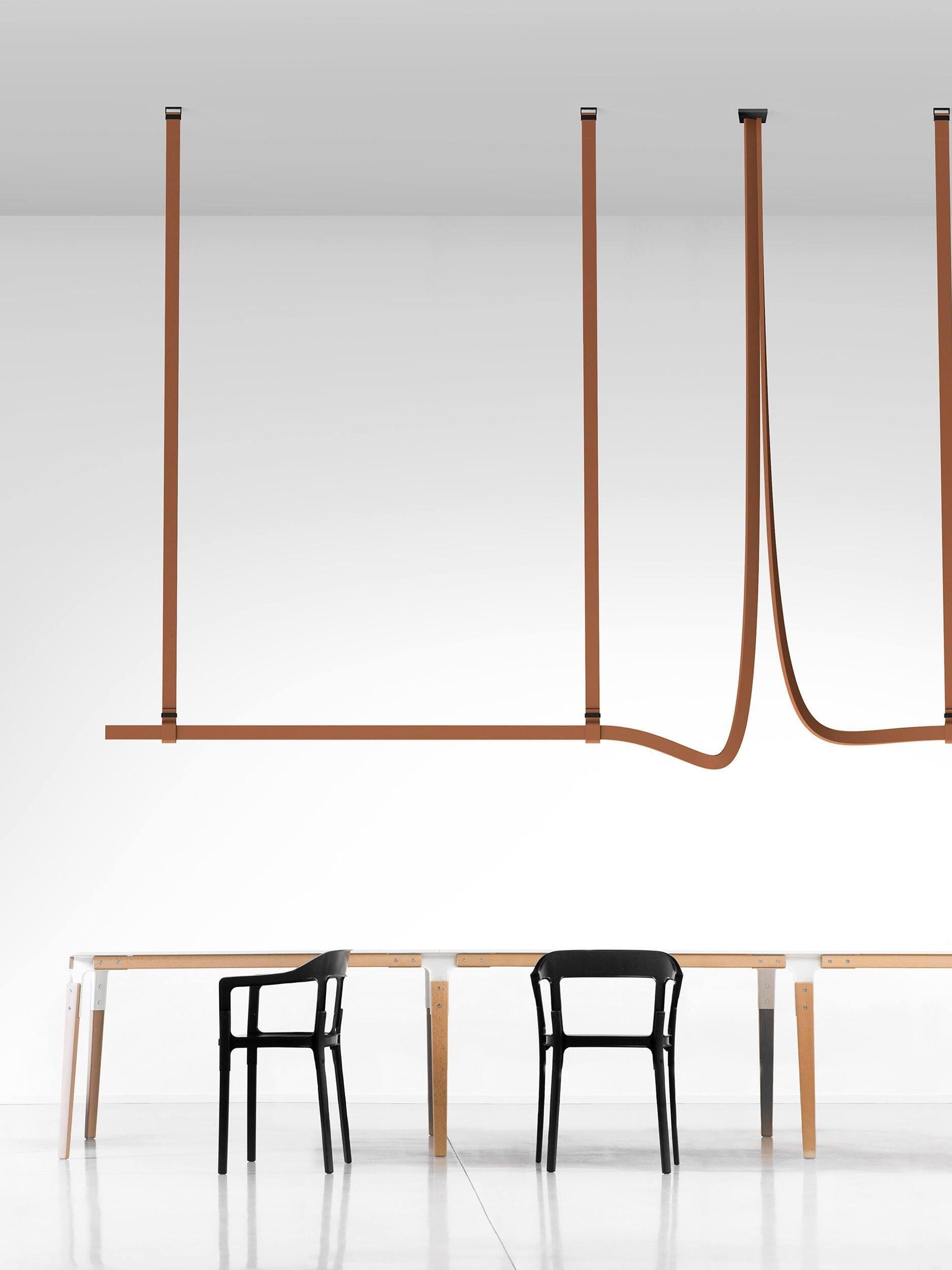 Extended brown belt-shaped arrangement with several ceiling straps and a curved return above pale tables and black chairs