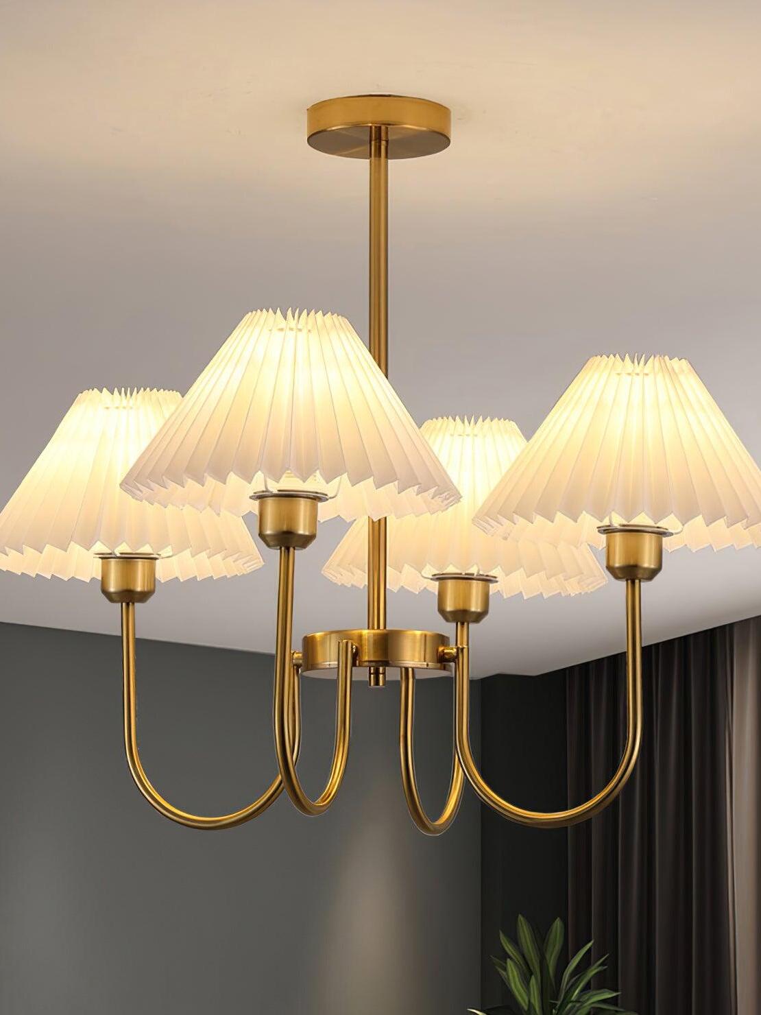 Illuminated pleated shades and curved chandelier arms near a dark wall and curtains