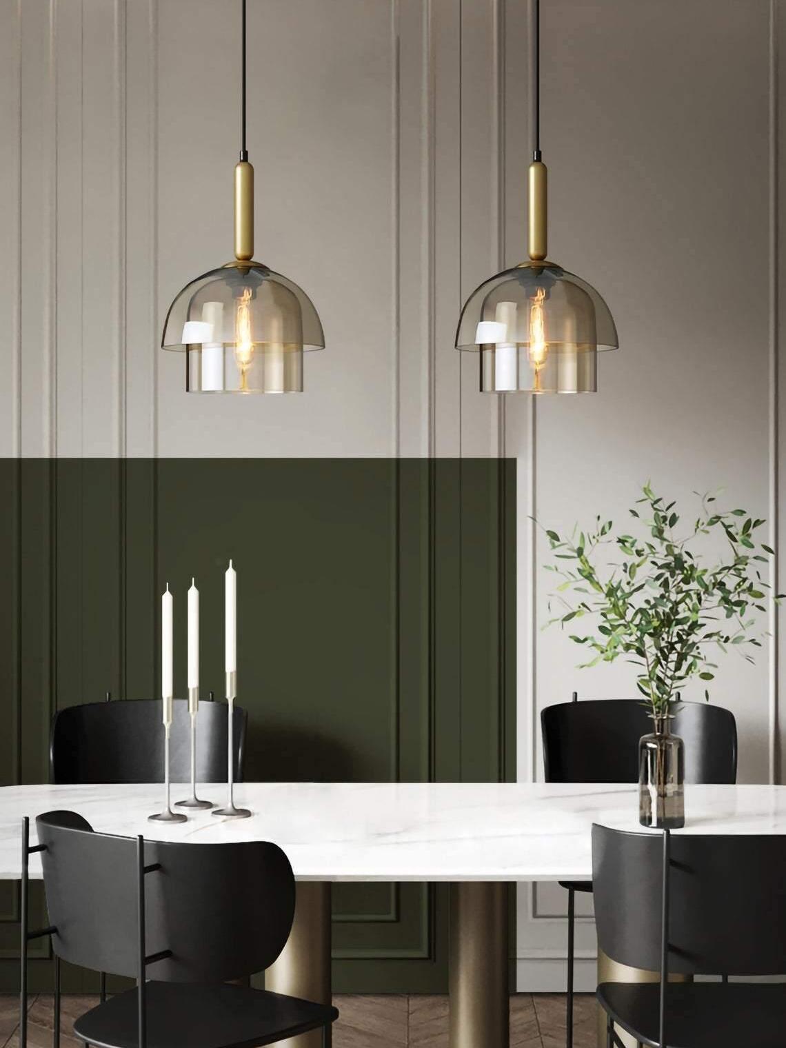 Two two-tier glass pendants above a white dining table with candlesticks, leafy branches, black chairs and panelled wall