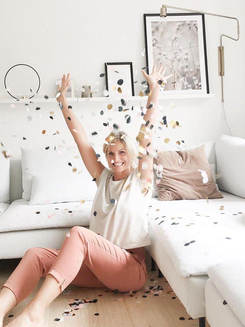 Brass-tone wall lamp above a white sofa with a seated woman throwing confetti in the foreground