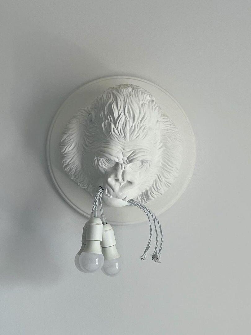 White sculpted gorilla face on grey background with pale holders and unlit bulbs
