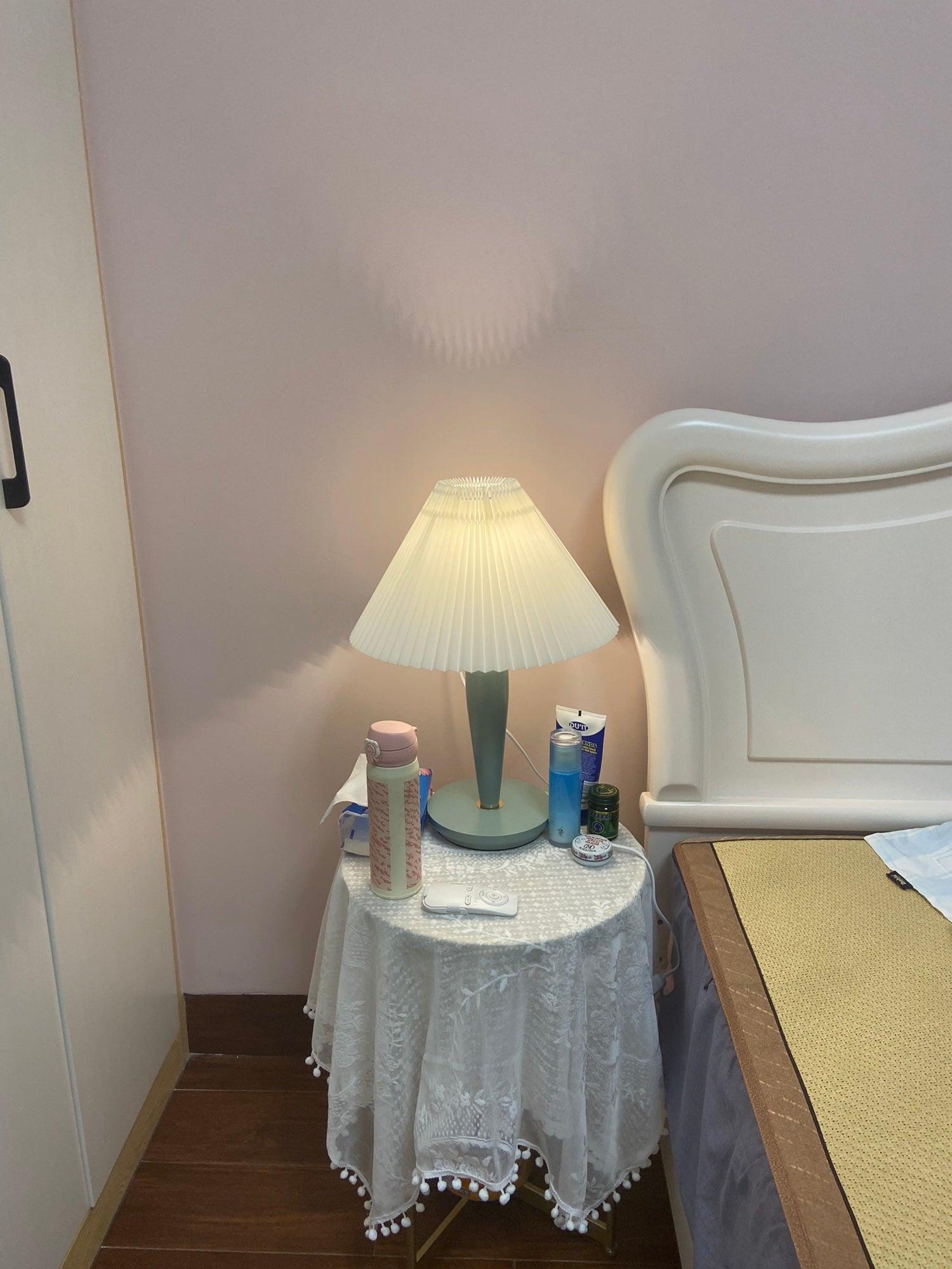 Light-blue lamp and white pleated shade beside bed