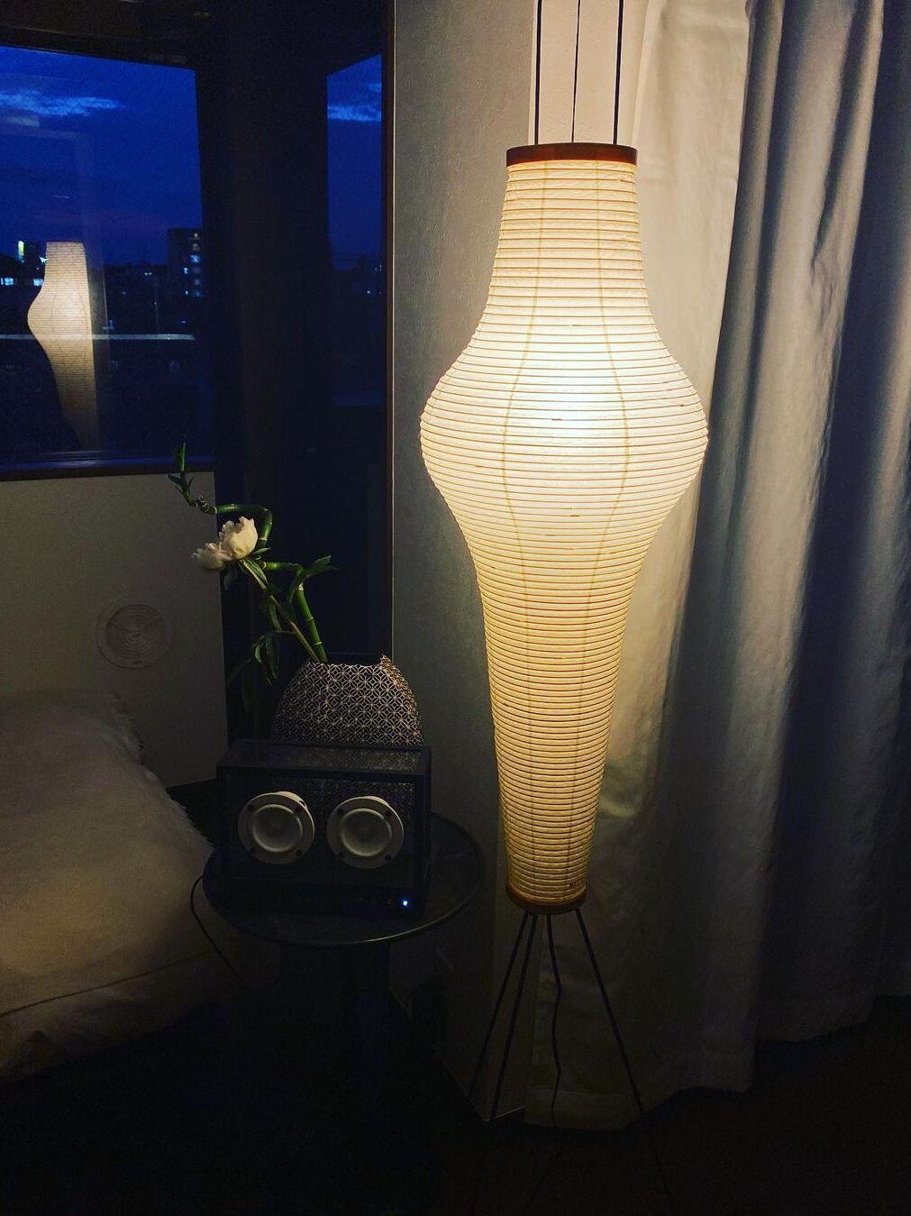 Tall glowing paper floor lamp near window at night