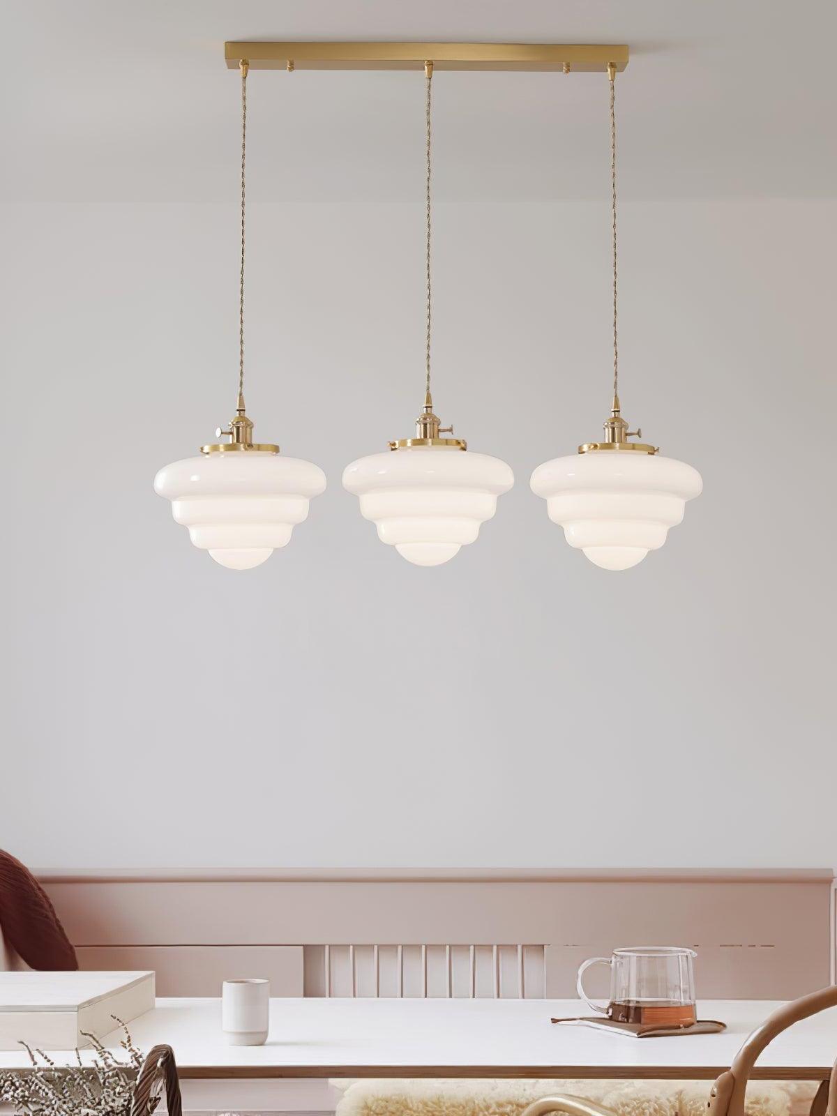 Atlas Model B three-head pendant with rounded white glass tiers and a brass canopy above a white table and pastel bench